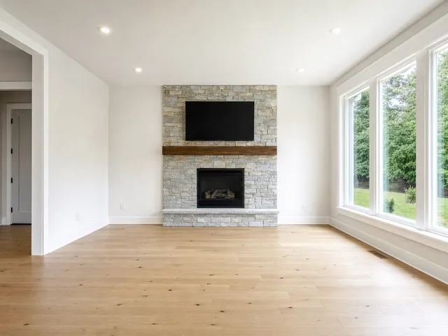 An empty living room with a stone fireplace and large windows, before AI virtual staging