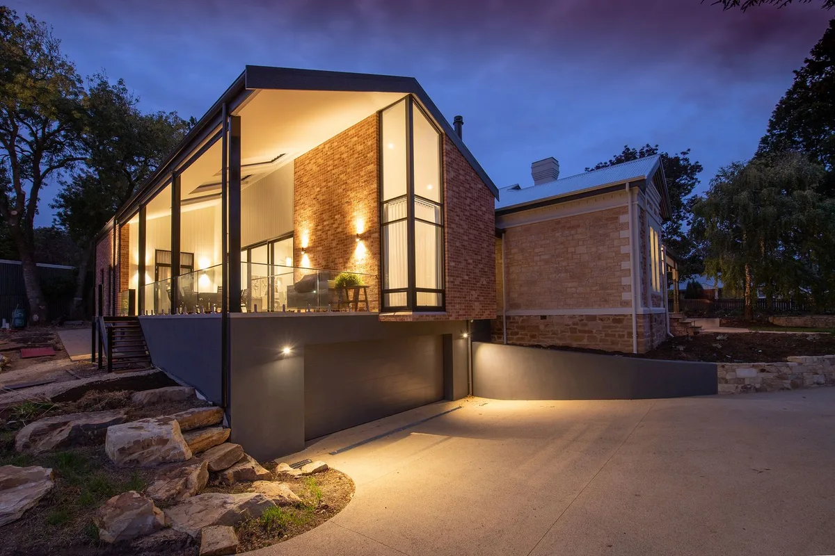 Modern brick home glowing with warm exterior lights at twilight against a dusk sky